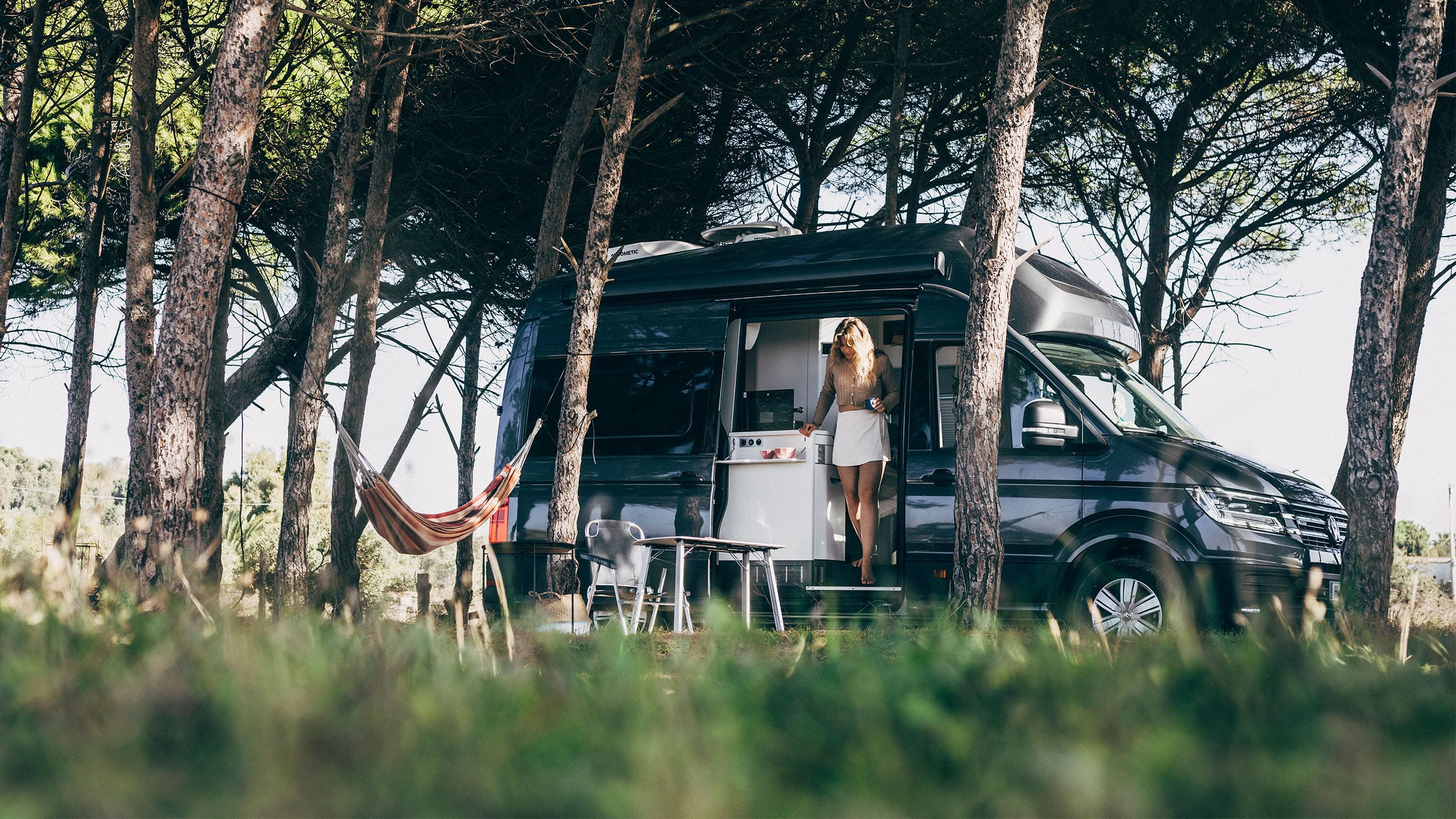 VW Grand California stoi pod drzewami.