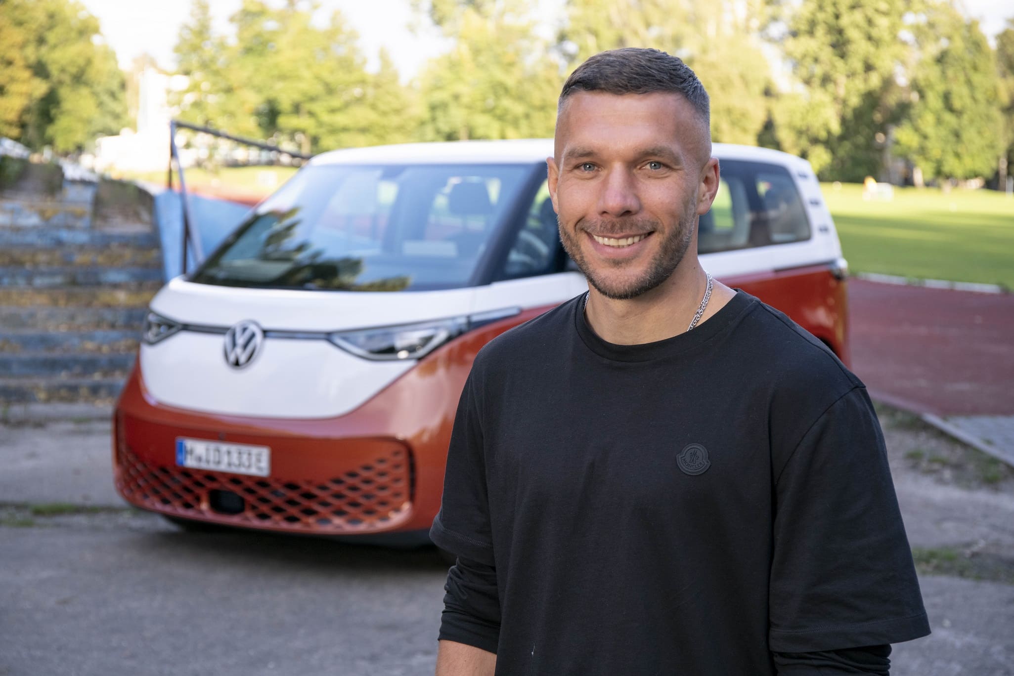 Lukas Podolski na tle Volkswagena ID. Buzz.