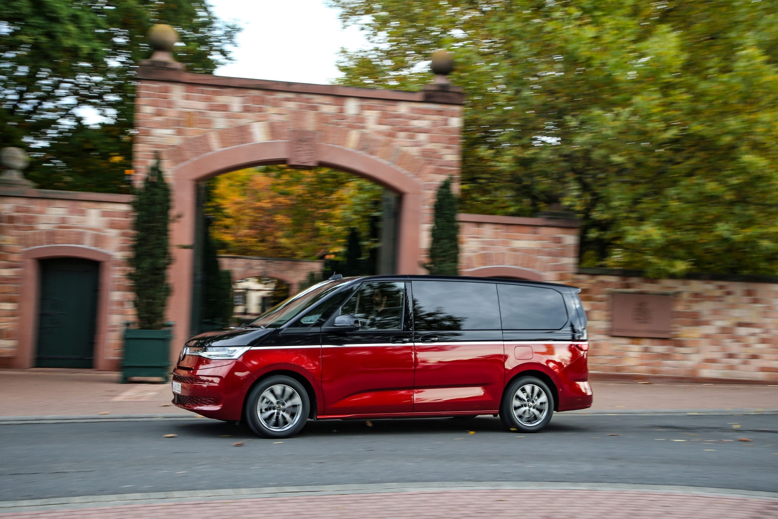 Volkswagen Multivan przejeżdża obok ceglanej bramy.