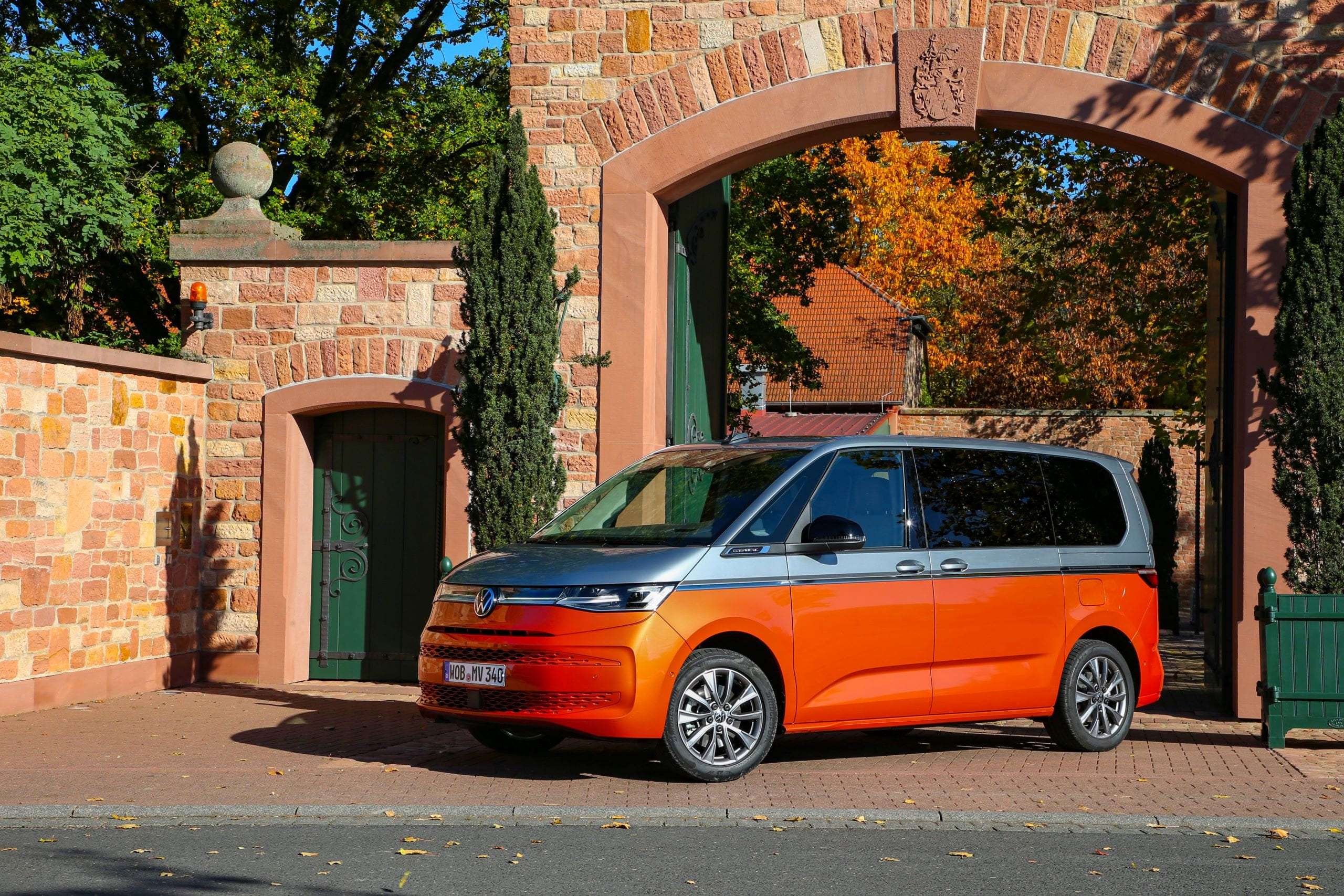 Szaro-pomarańczowy Volkswagen Multivan stoi na tle ceglanej bramy.
